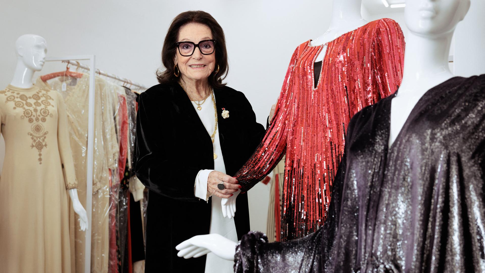 Nana Mouskouri posiert zwischen Kleiderpuppen und Kleiderständern mit verschiedenen Bühnen-Kleidern der Sängerin.