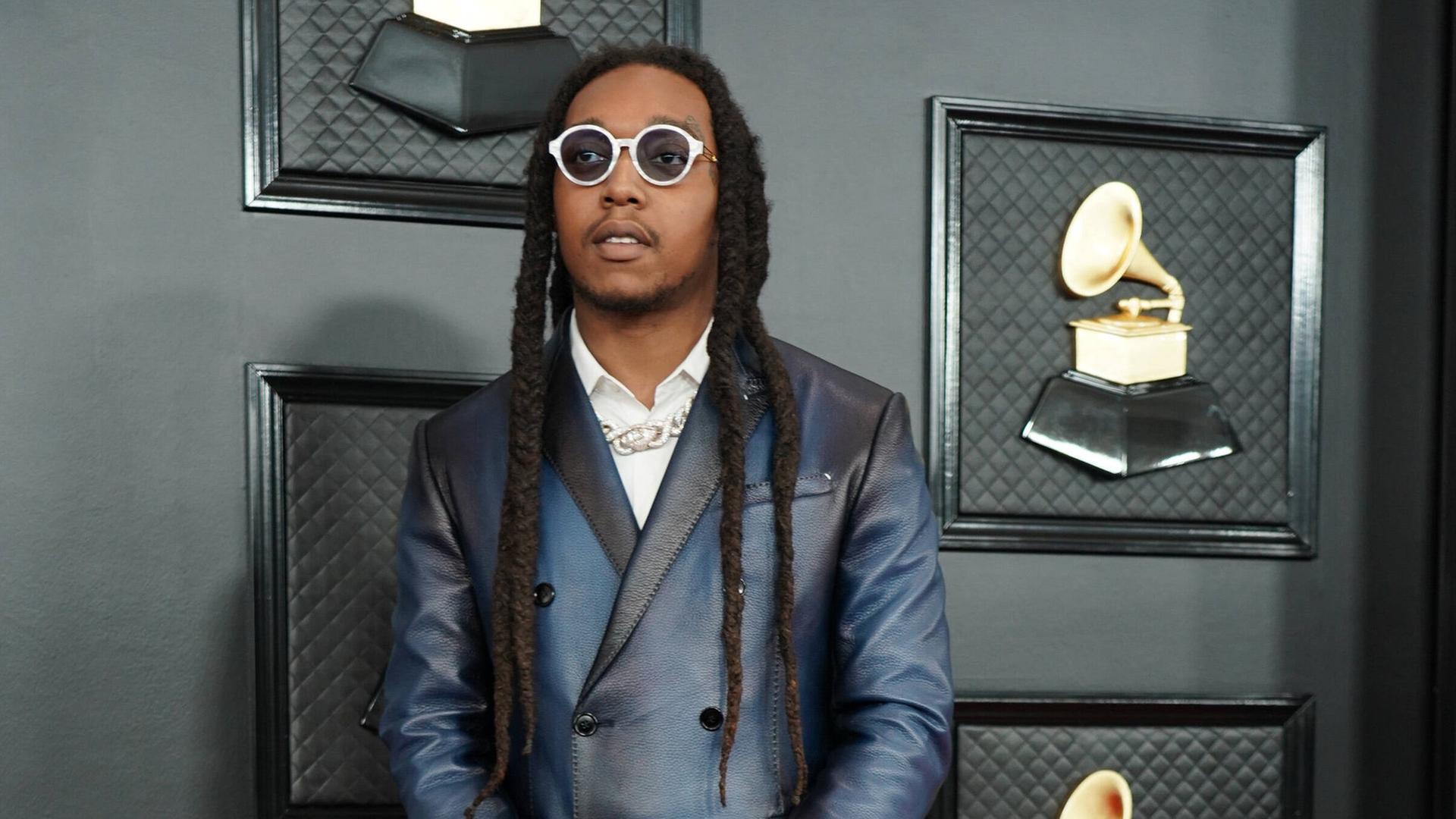 Migos, einer der Rapper von Takeoff, steht vor einer Wand mit Bildern von Grammys. Migos, einer der Rapper von Takeoff, steht vor einer Wand mit Bildern von Grammys.