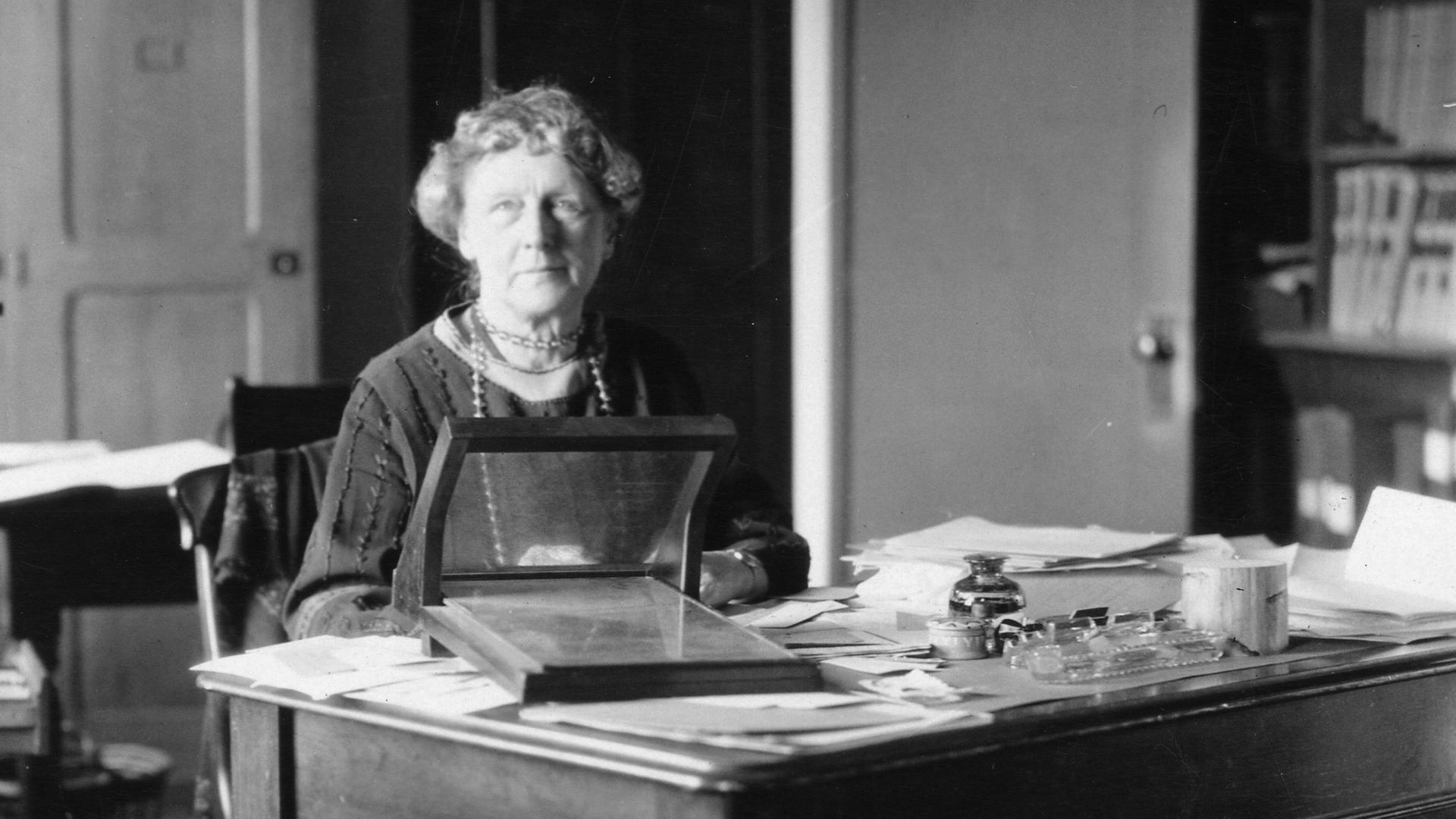 Die große Astronomin Annie Jump Cannon (1863-1941) begründete die physikalische Erforschung der Sterne. Auf einer Schwarz-Weiß-Aufnahme sitzt sie als ältere Dame an einem Tisch mit Instrumenten.