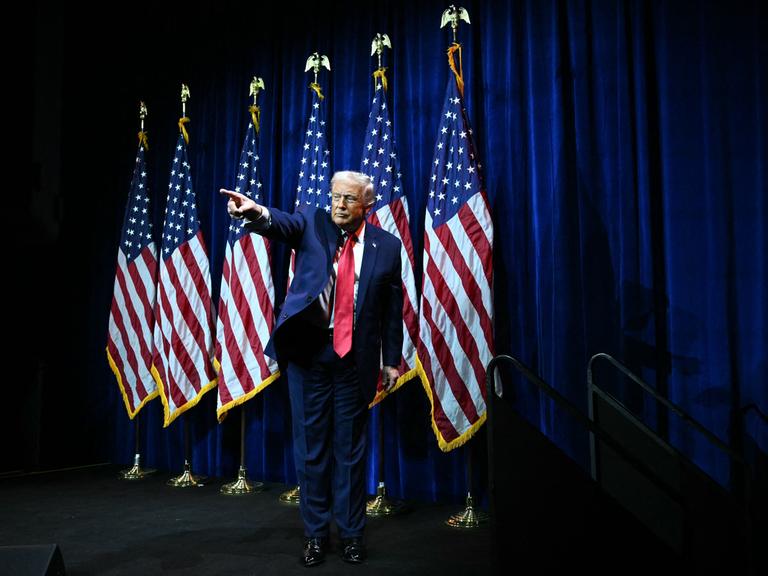 Donald Trump steht auf einer Bühne vor US-Flaggen und zeigt mit ausgestrecktem Arm und Zeigefinger ins Publikum.