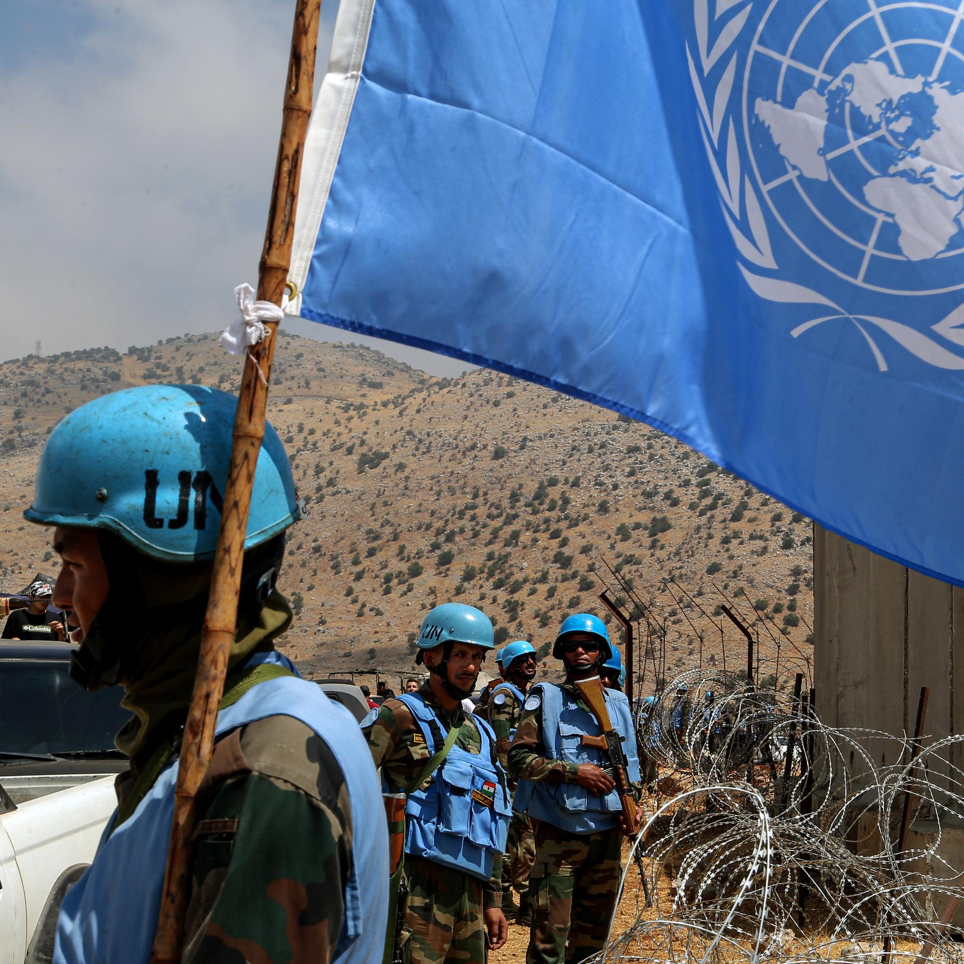 UNO-Friedenstruppen mit blauen Helmen an der libanesischen Grenze zu Israel. Im Vordergrund eine Flagge der Vereinten Nationen.