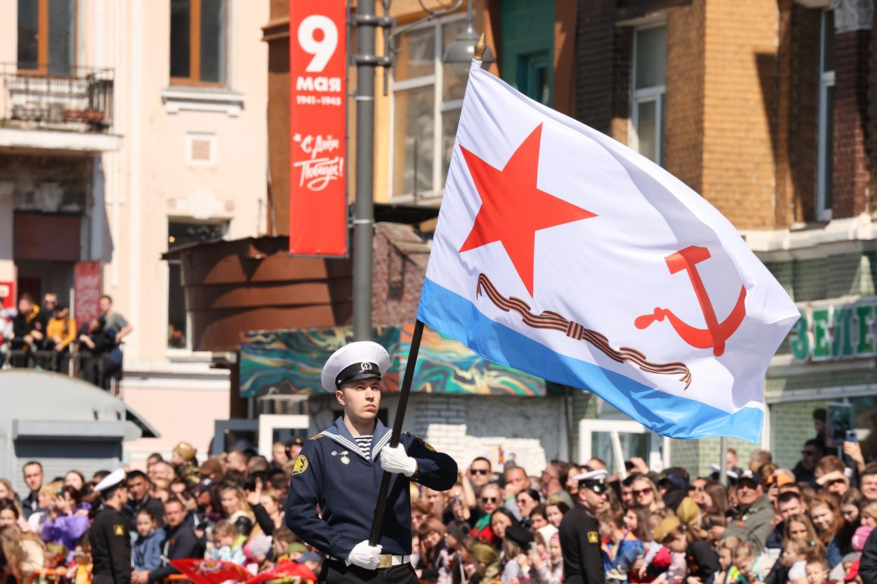 Ein Marineinfanterist schwingt bei der Siegesparade in Wladiwostok eine Fahne mit einem roten Stern und Hammer und Sichel darauf.