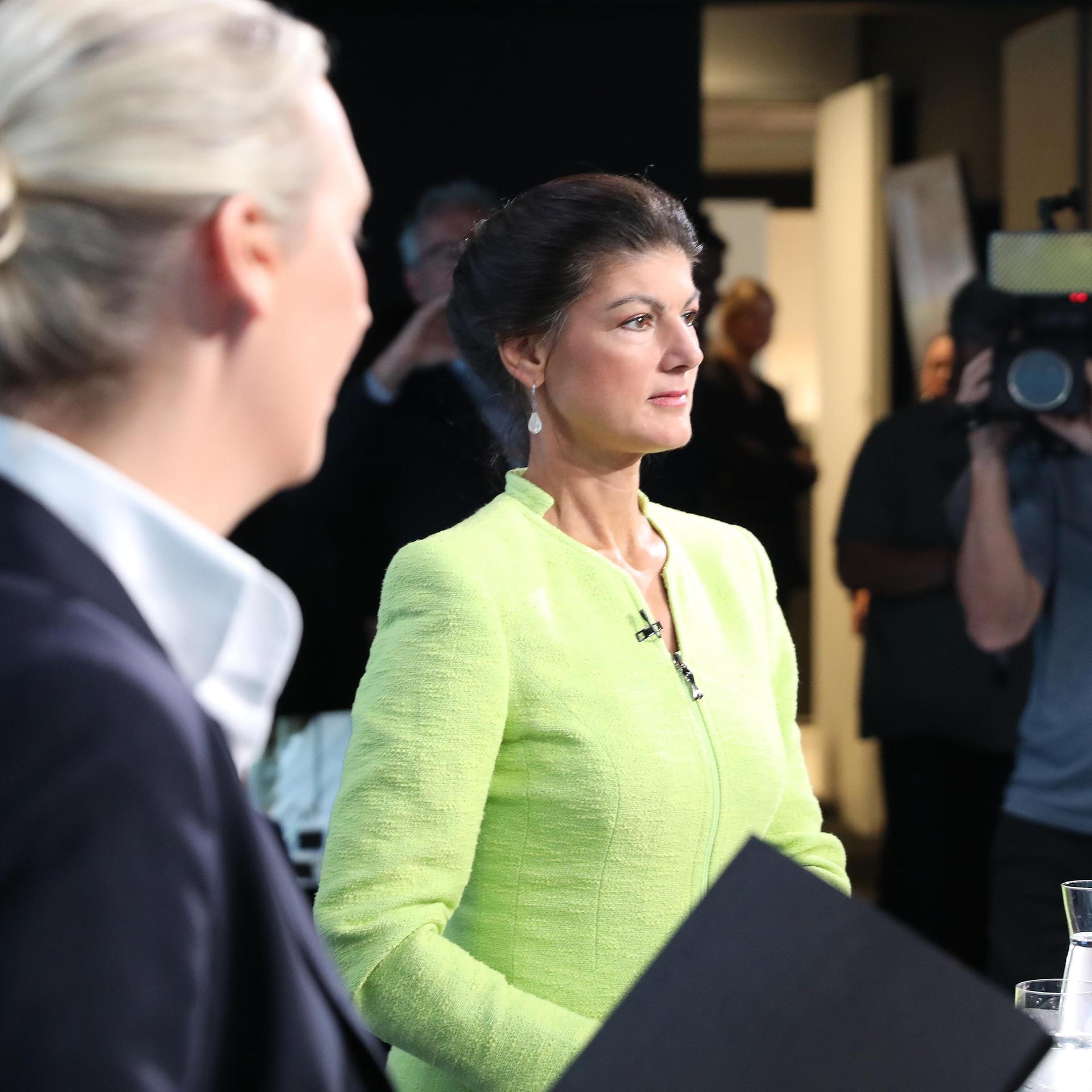 Alice Weidel steht mit ihrem Kopf von der Kamera zu Sahra Wagenknecht auf der Seite, die in einer gelben Green -Jacke auf die Vorderseite schaut. Das Foto wurde im World TV Studio aufgenommen.