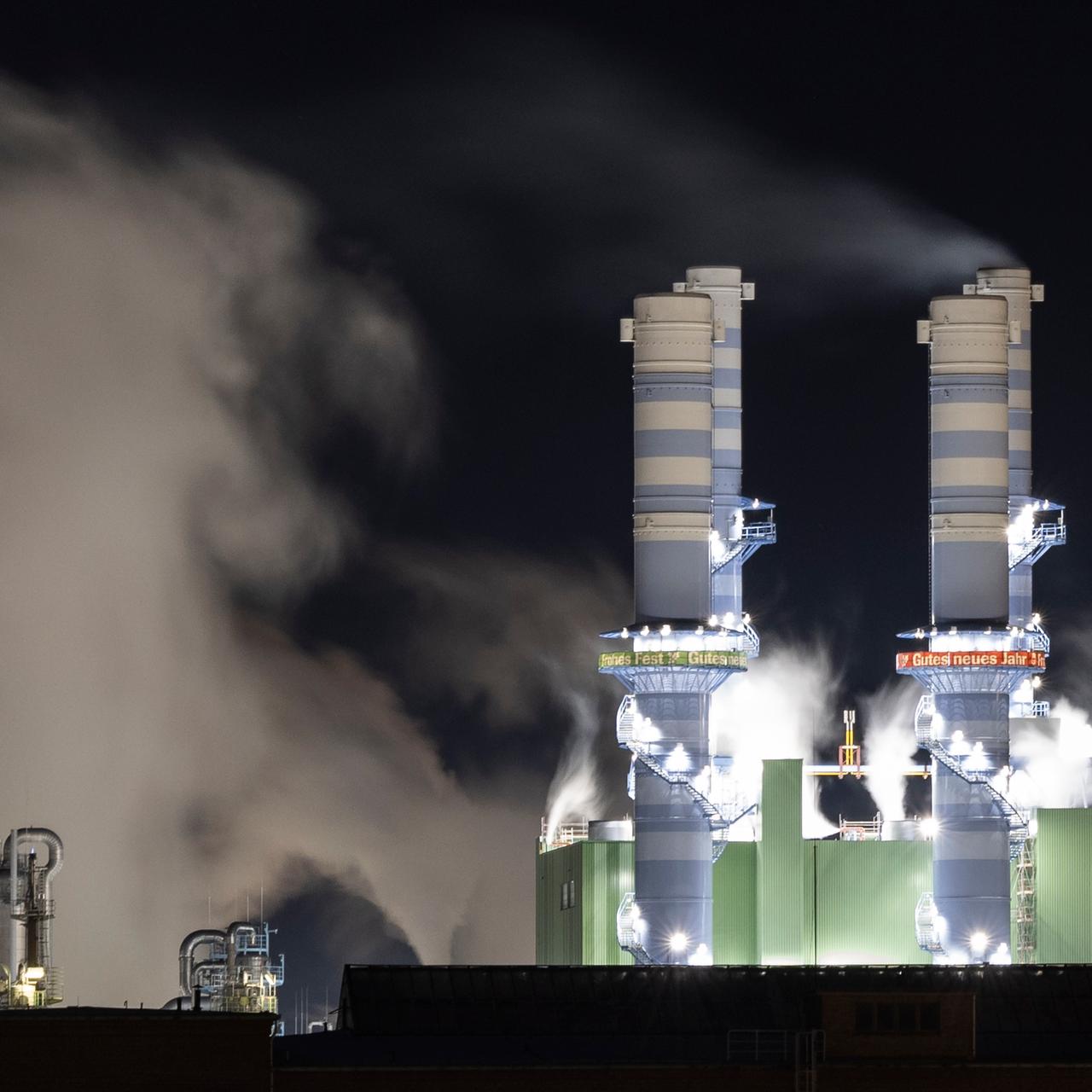 Dampf steigt bei Nacht aus beleuchteten Industrieschornsteinen des Industriepark Höchst auf. 
