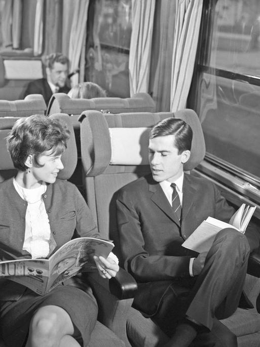 Zugreisen in den 1960er Jahren - ein Paar sitzt im Zug, die Frau eine Zeitschrift, der Mann ein Buch lesend.