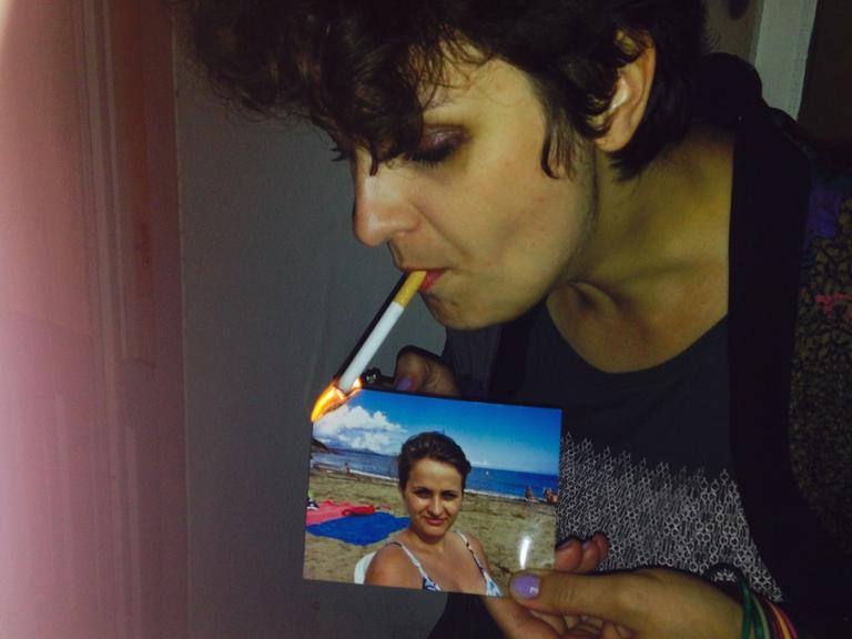 Eine Frau zündet mit ihrer Zigarette ein Bild von sich aus der Vergangenheit an.