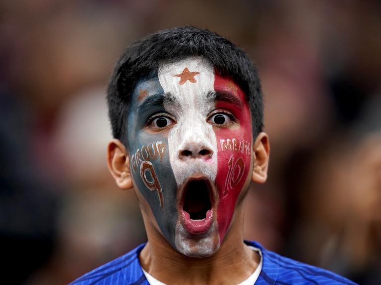 Ein junger Fan jubelt. Sein Gesicht ist mit den Farben der französischen Flagge bemalt.