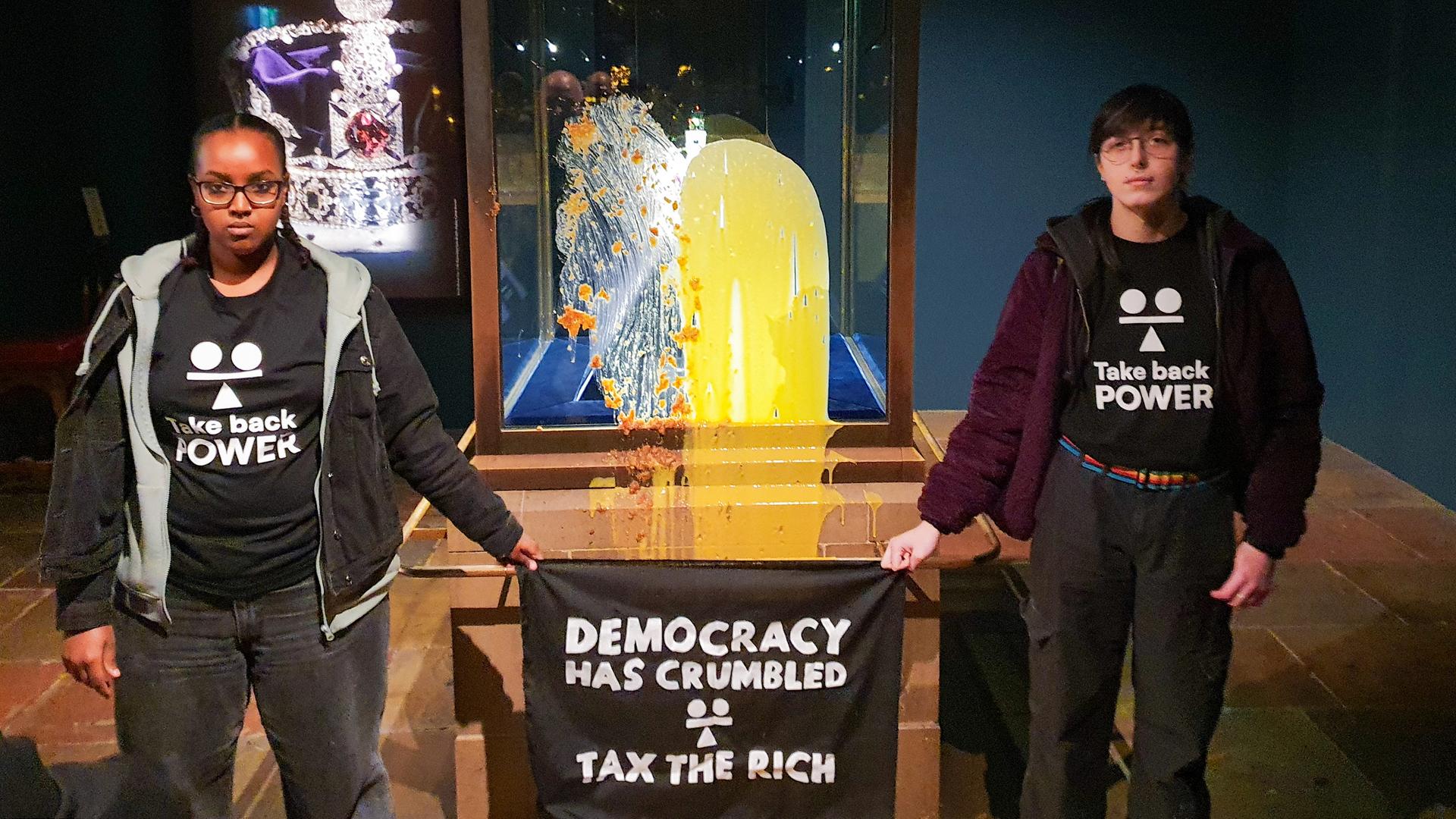 Aktivisten im Tower of London nach einer "Lebensmittelattacke" auf die Kronjuwelen - sie haben Shirts mit der Aufschrift "Take back Power" an und halten ein Transparent in den Händen auf dem steht "Tax the rich" - also "Besteuer die Reichen". Aktivisten im Tower of London nach einer "Lebensmittelattacke" auf die Kronjuwelen - sie haben Shirts mit der Aufschrift "Take back Power" an und halten ein Transparent in den Händen auf dem steht "Tax the rich" - also "Besteuer die Reichen".