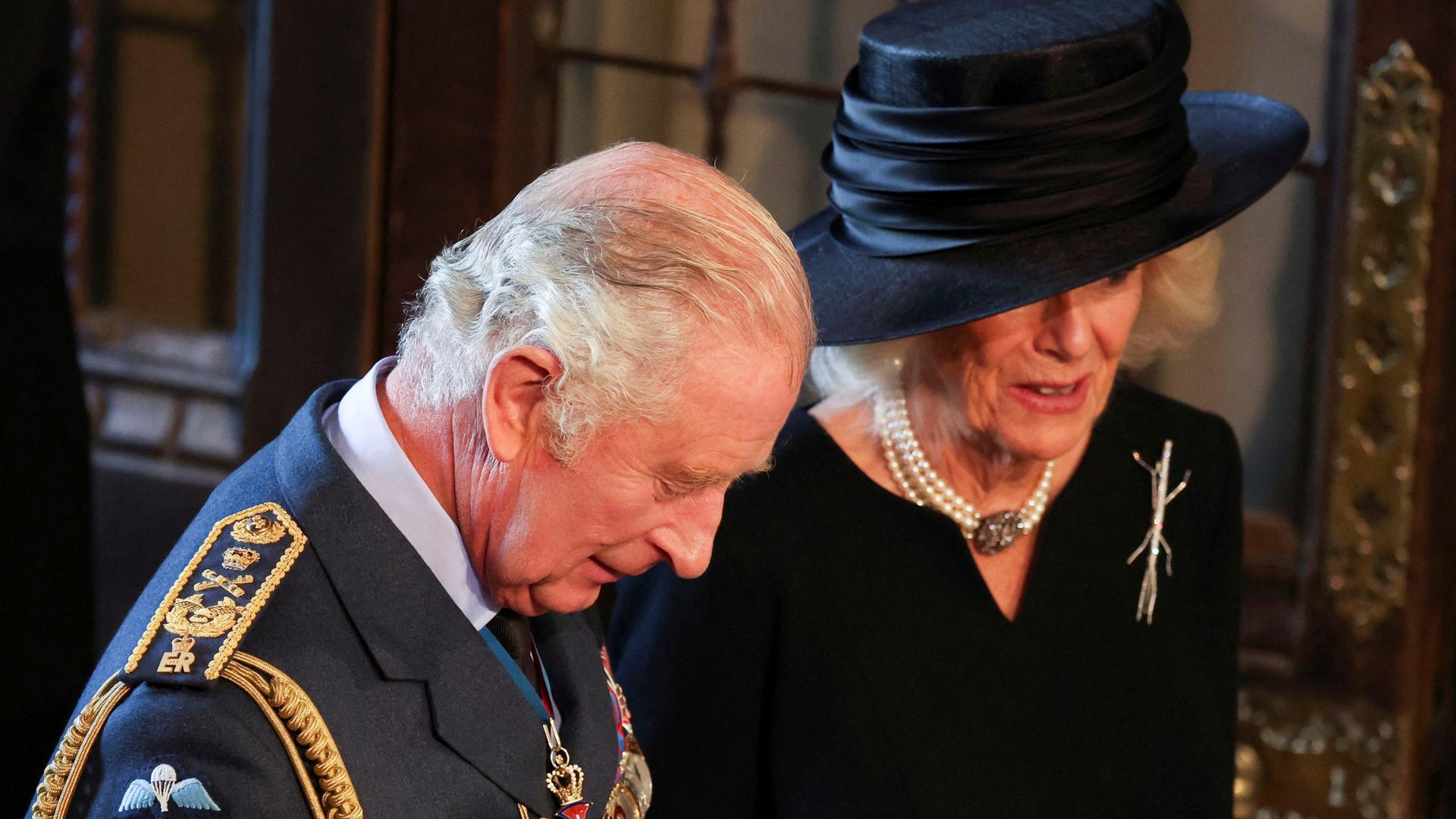 König Charles und Camilla stehen nebeneinander, Charles trägt eine Uniform, er senkt den Koppf. Camilla trägt ein schwarzes Kleid und einen schwarzen Hut. König Charles und Camilla stehen nebeneinander, Charles trägt eine Uniform, er senkt den Koppf. Camilla trägt ein schwarzes Kleid und einen schwarzen Hut.