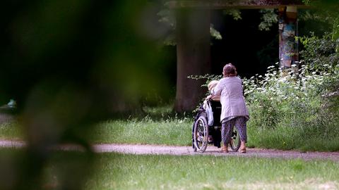 Eine ältere Dame schiebt eine Person in einem Rollstuhl durch einen Park. 