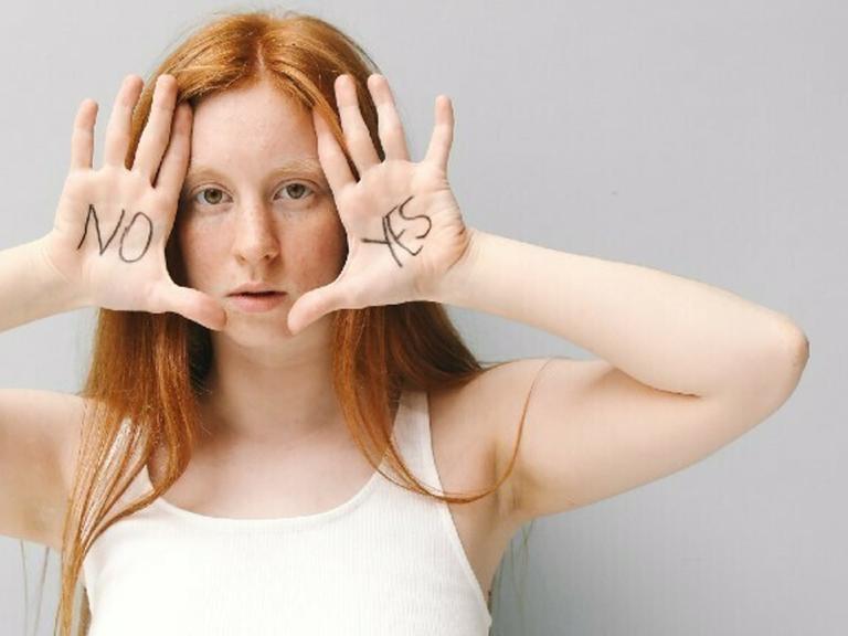 Eine Frau hält ihre Hände an das Gesicht. Auf einer Hand steht "Nein" auf der anderen "Ja".