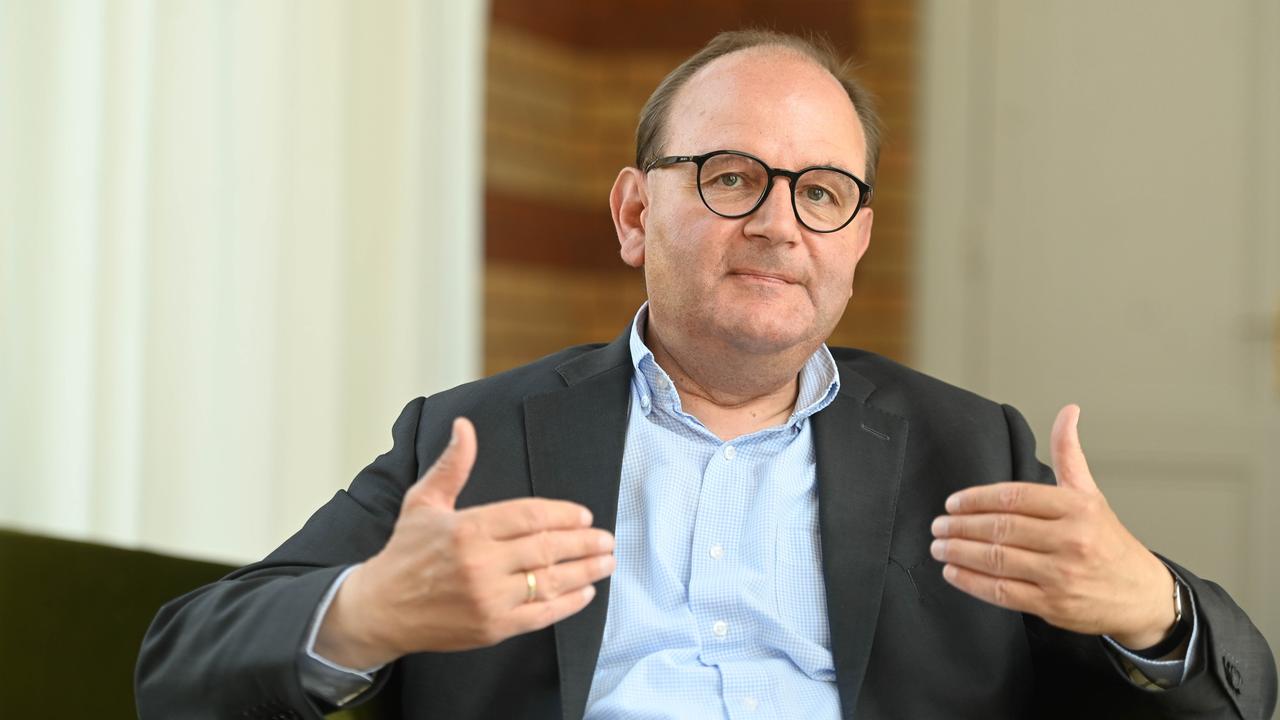 Ottmar Edenhofer vom Potsdam-Institut für Klimafolgenforschung zeigt mit beiden Händen auf sich. Er trägt eine Brille, einen Anzug und ein blaues Hemd.