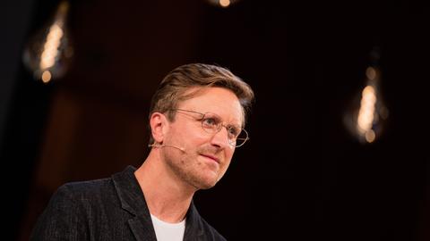 Carl Gierstorfer vor dunklem Hintergrund. Er trägt ein dunkles Jacket und eine schwarze Brille.