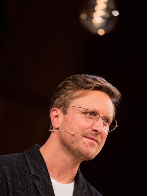 Carl Gierstorfer vor dunklem Hintergrund. Er trägt ein dunkles Jacket und eine schwarze Brille.