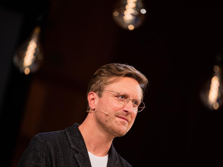 Carl Gierstorfer vor dunklem Hintergrund. Er trägt ein dunkles Jacket und eine schwarze Brille.