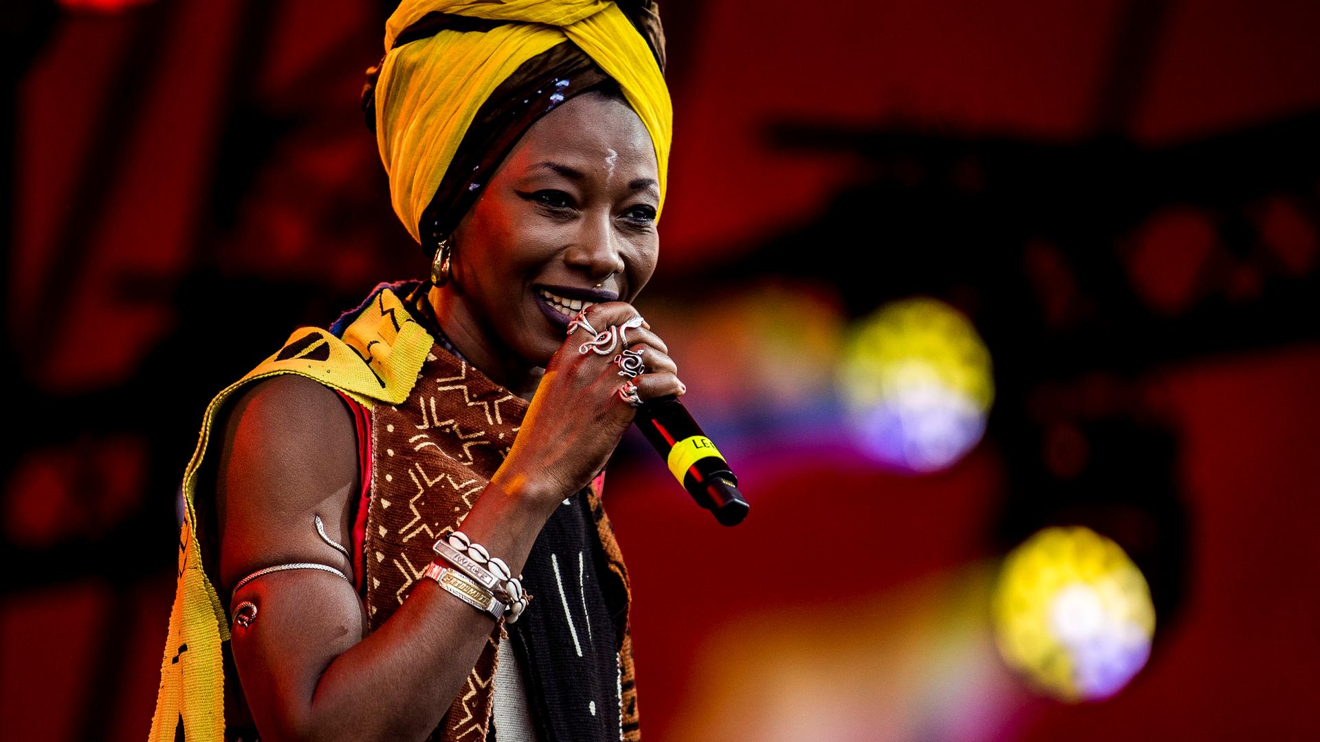 Fatoumata Diawara seht mit Schmuck ihrer Heimat und einem gelben Haartuch auf der Bühne und singt.