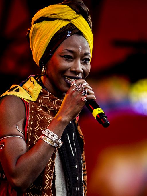 Fatoumata Diawara seht mit Schmuck ihrer Heimat und einem gelben Haartuch auf der Bühne und singt.