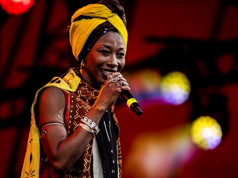 Fatoumata Diawara seht mit Schmuck ihrer Heimat und einem gelben Haartuch auf der Bühne und singt.
