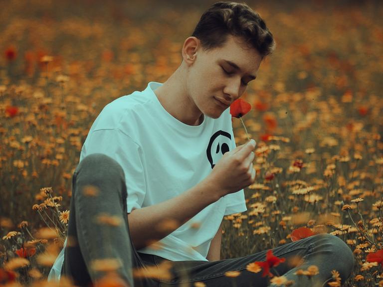 Junger Mann riecht an einer Blume.