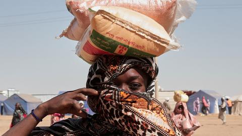 Eine sudanesische Geflüchtete mit Kopftuch trägt Säcke mit Nahrungsmitteln auf dem Kopf