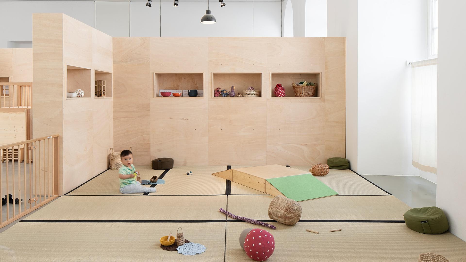 Ein Kleinkind sitzt in der Installation "Eltern und Kleinkinder Krippe" umgeben von Spielzeug.