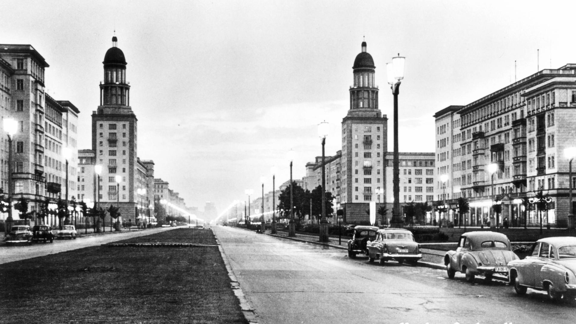 Schwarzweißaufnahme der Stalinallee: Der breite Boulevard ist von Kächelgebäuden im klassizistischen Stil gesäumt.
