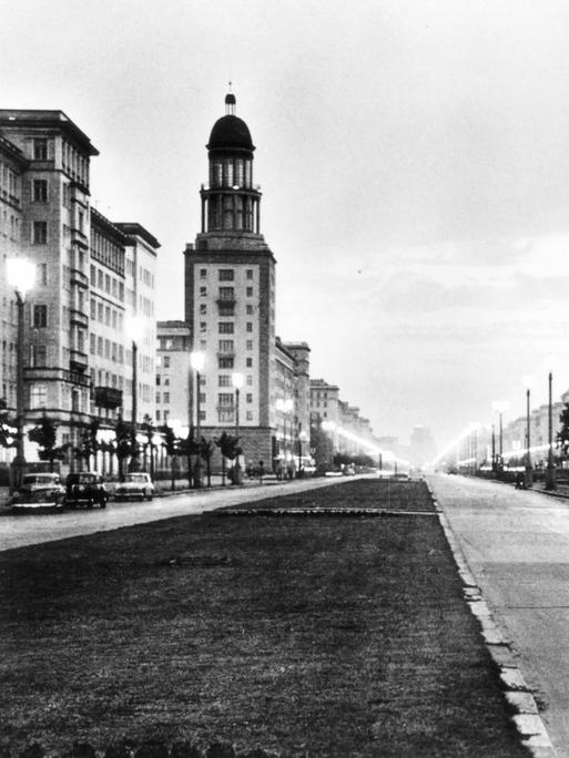 Schwarzweißaufnahme der Stalinallee: Der breite Boulevard ist von Kächelgebäuden im klassizistischen Stil gesäumt.