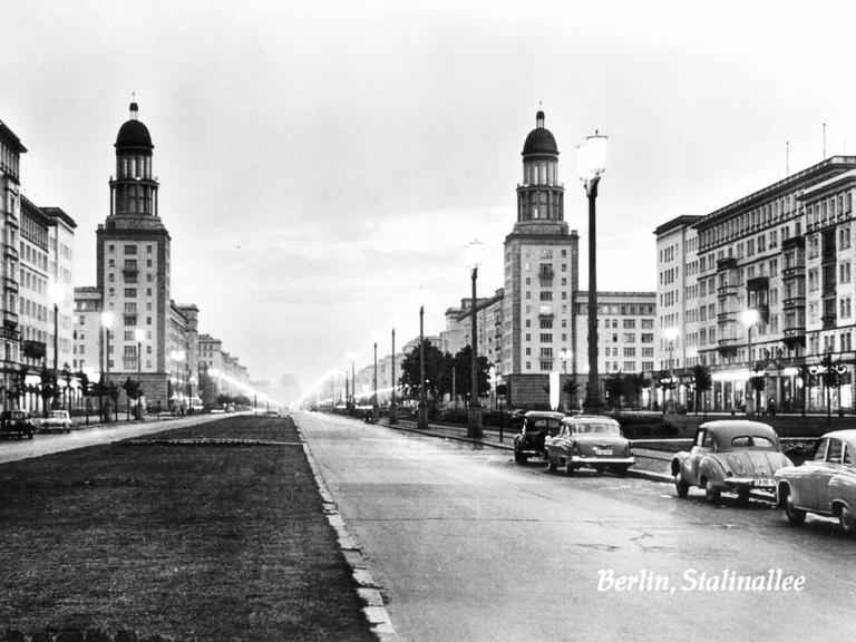 Schwarzweißaufnahme der Stalinallee: Der breite Boulevard ist von Kächelgebäuden im klassizistischen Stil gesäumt.