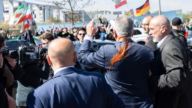 Reza Pahlavi hat Tomaten-Saft am Rücken und am Hals. Er winkt seinen Anhängern zu.