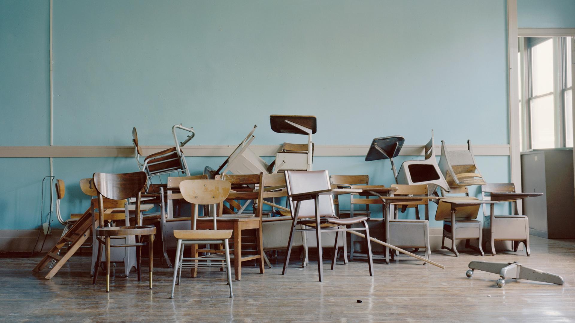 Alte Stühle liegen in einem leeren Klassenraum herum.