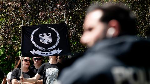 Junge Menschen tragen eine Fahne mit dem Logo der Deutschen Jugend Voran (DJV), ein weißer Adler auf schwarzem Grund, umringt von einem Eichenkranz, im Vordergrund eine verschwommene Person mit einem schwarzen Hoodie
