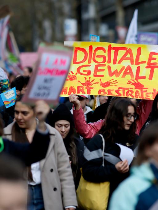 Demonstranten stehen dicht gedrängt auf der Straße und halten Schilder in die Höhe. Auf einem Schild steht "Digitale Gewalt hart bestrafen" in Rot auf Gelb.