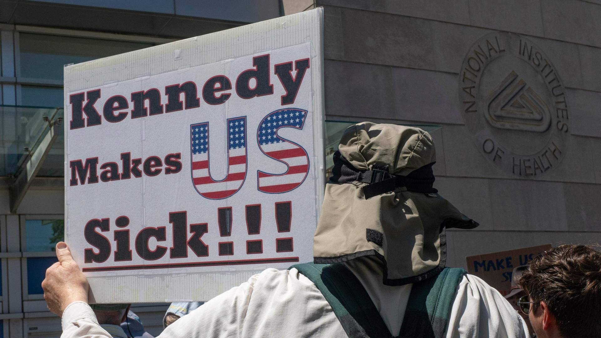 Ein Demonstrant hält ein Schild mit der Aufschrift "Kennedy Makes US Sick!!!". Ein Demonstrant hält ein Schild mit der Aufschrift "Kennedy Makes US Sick!!!".