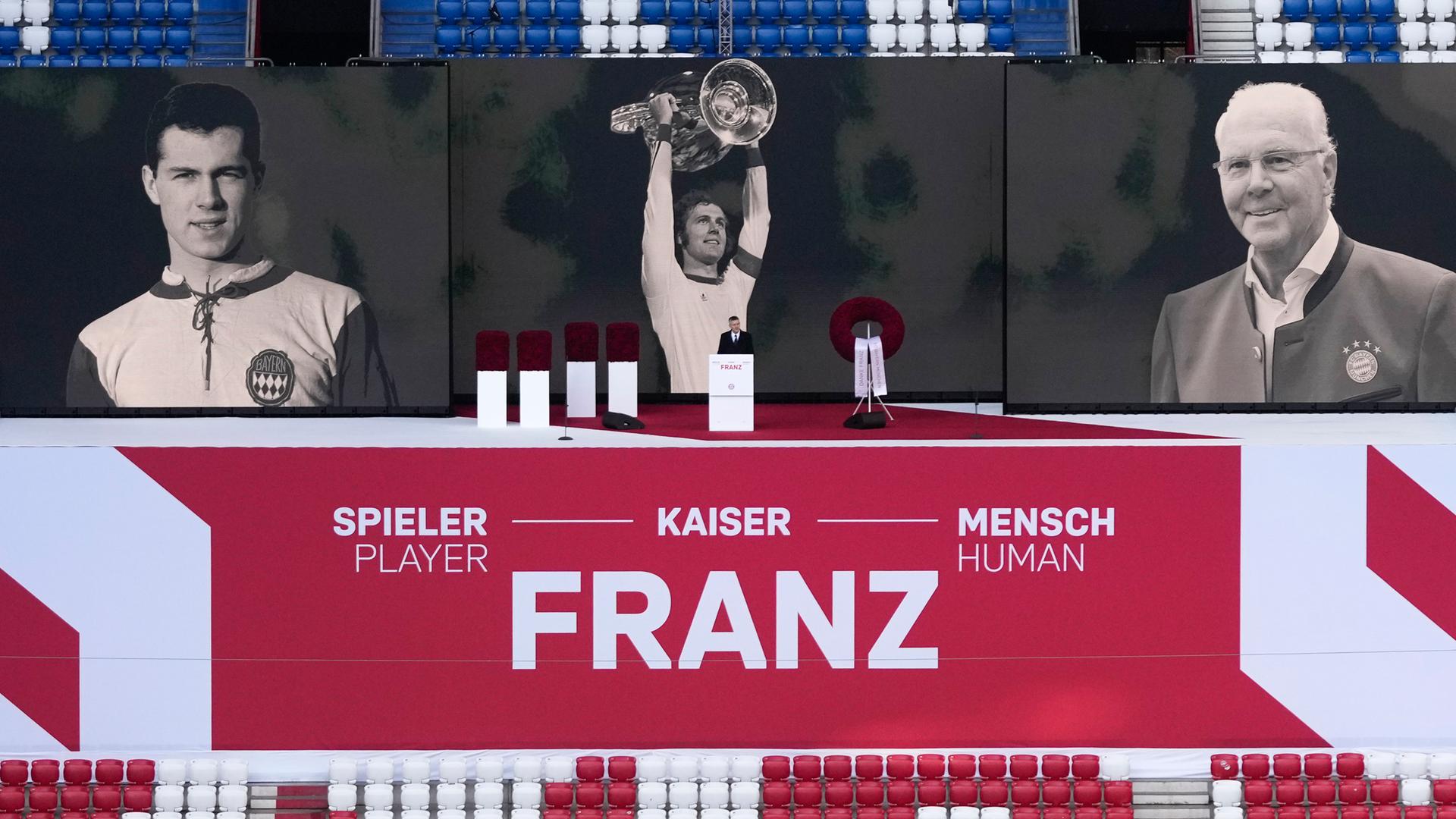 Bild von der Gedenk-Feier: Über den Sitzen im Stadion ist ein großes Plakat. Darauf steht "Spieler - Kaiser - Mensch". Außerdem sind darauf Schwarz-Weiß-Fotos von Franz Beckenbauer als er jung war und als er alt war.