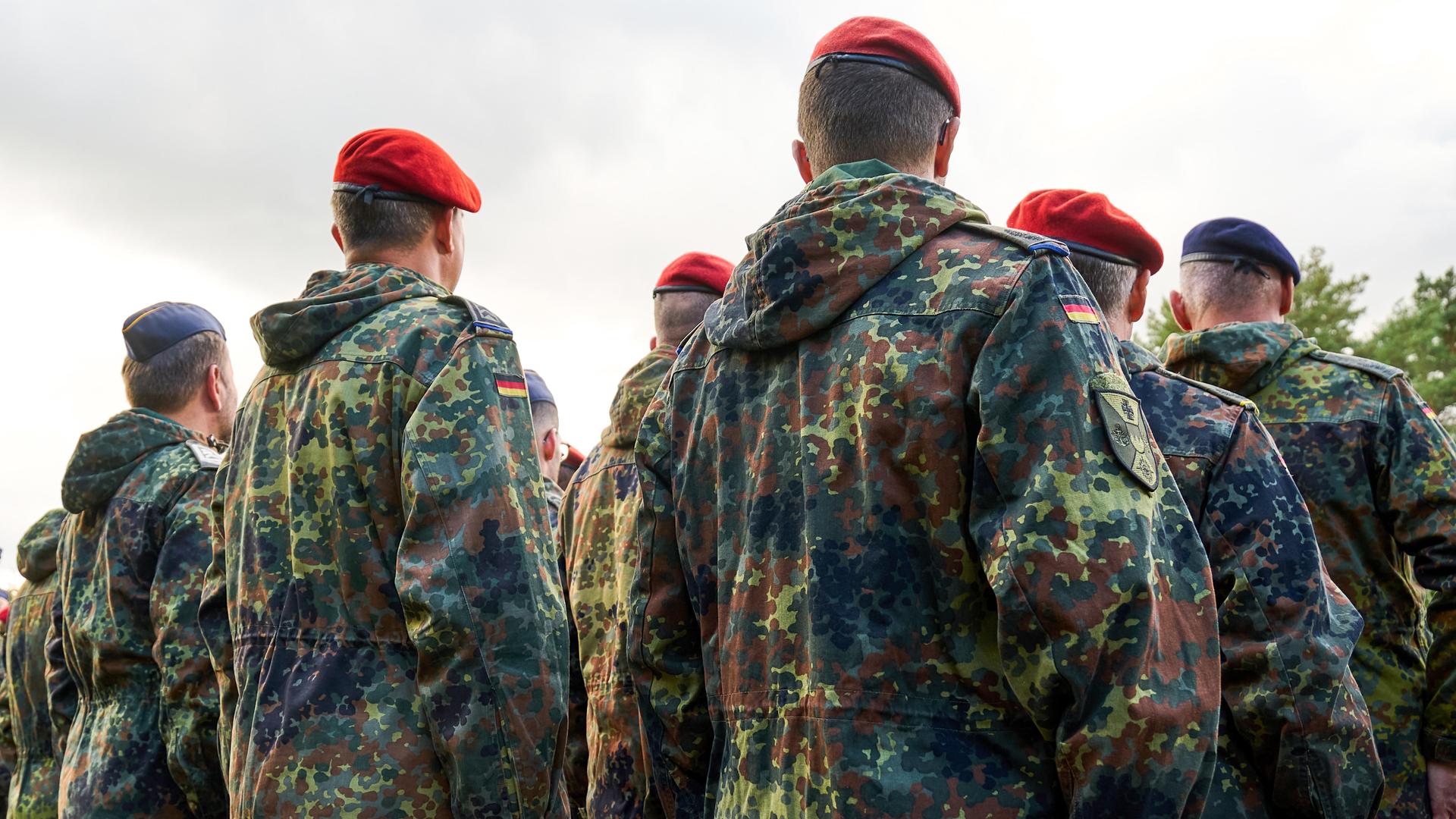 Soldaten der Bundeswehr stehen in Reih und Glied, gekleidet in Flecktarnuniformen und tragen rote Baretts