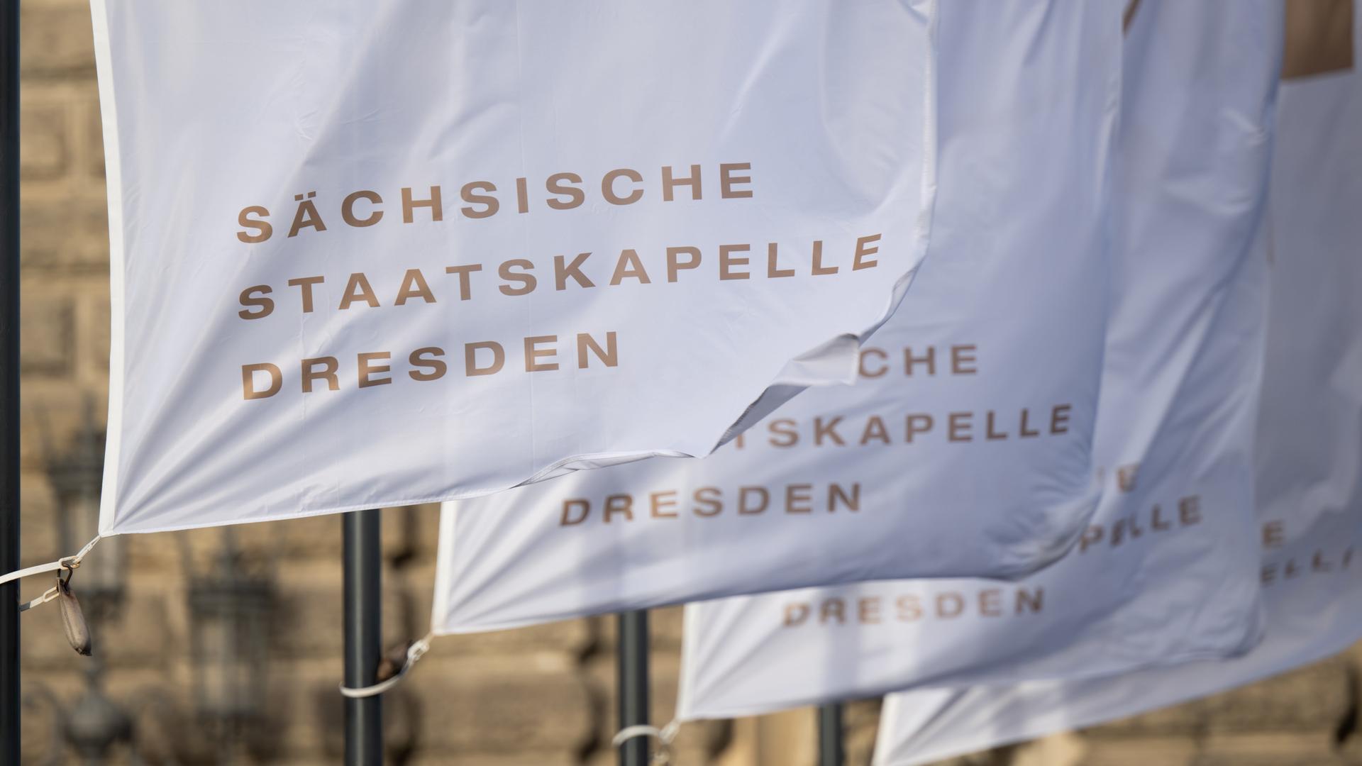Fahnen mit der Aufschrift "Sächsische Staatskapelle Dresden" wehen vor der Semperoper im Wind. Fahnen mit der Aufschrift "Sächsische Staatskapelle Dresden" wehen vor der Semperoper im Wind.