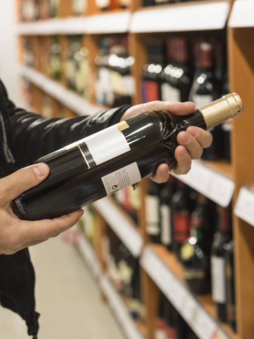 Ein Kunde liest das Etikett einer Weinflasche im Supermarkt