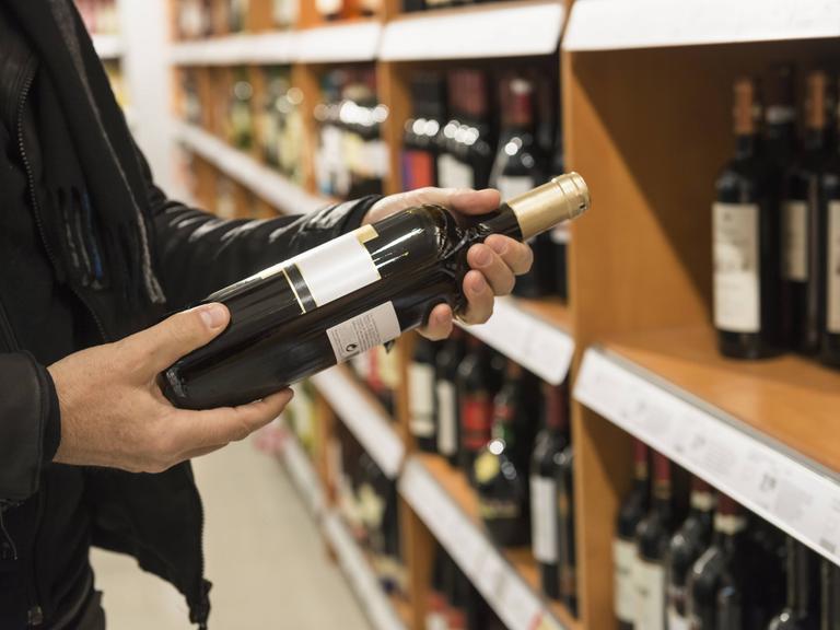 Ein Kunde liest das Etikett einer Weinflasche im Supermarkt