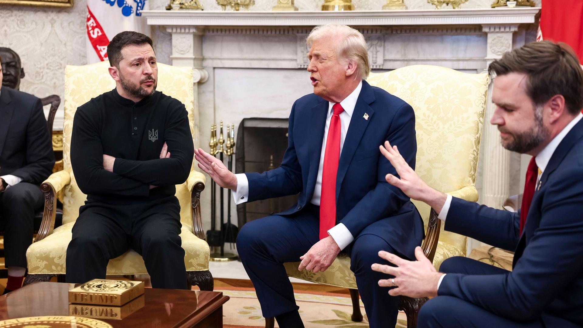 Eine Pressekonferenz im Weißen Haus in Washington. Links auf einem Sessel sitzt der ukrainische Präsident Wolodymyr Selenskyj mit verschränkten Armen, rechts von ihm gestikulieren Präsident Donald Trump und Vize-Präsident J. D. Vance mit erhobenen Händen.