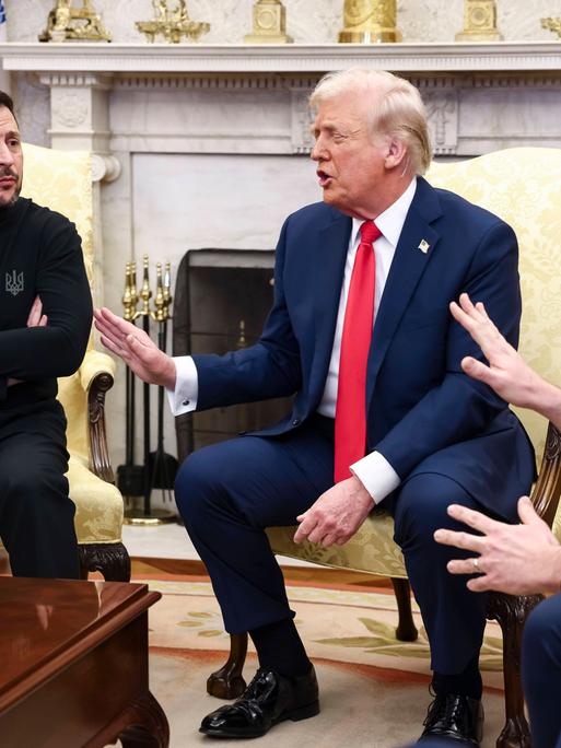 Eine Pressekonferenz im Weißen Haus in Washington. Links auf einem Sessel sitzt der ukrainische Präsident Wolodymyr Selenskyj mit verschränkten Armen, rechts von ihm gestikulieren Präsident Donald Trump und Vize-Präsident J. D. Vance mit erhobenen Händen.