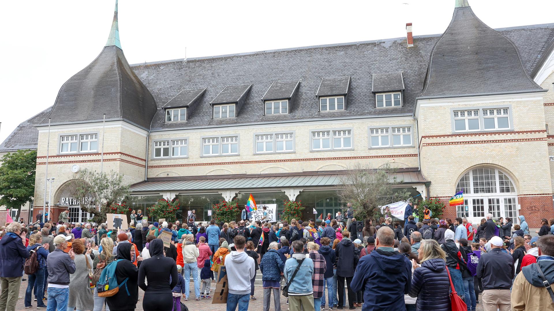 Teilnehmer stehen vor dem Rathaus in Westerland. Einige halten Transparente oder Regenbogenfahnen.