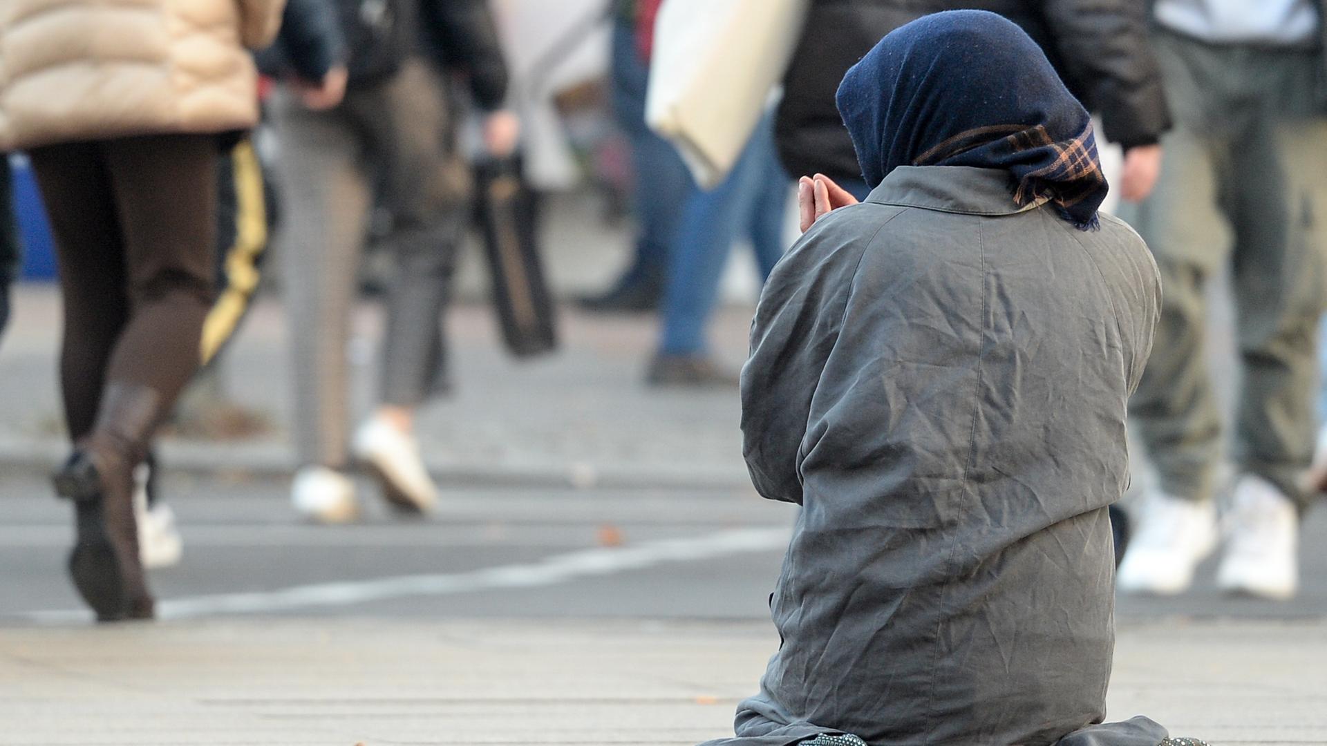 Eine Frau, die man nur von hinten sieht, bettelt inmitten vorbeilaufender Passanten. Eine Frau, die man nur von hinten sieht, bettelt inmitten vorbeilaufender Passanten.