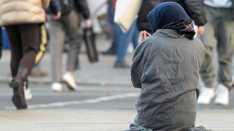Eine Frau, die man nur von hinten sieht, bettelt inmitten vorbeilaufender Passanten. 