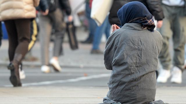 Eine Frau, die man nur von hinten sieht, bettelt inmitten vorbeilaufender Passanten. 
