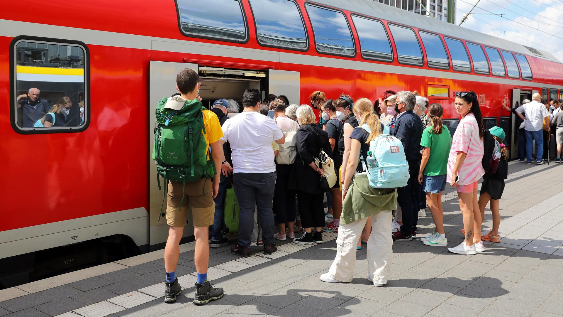 Fahr-Gäste warten in einer Schlange am Bahn-Steig auf den Einstieg in den Regional-Zug.