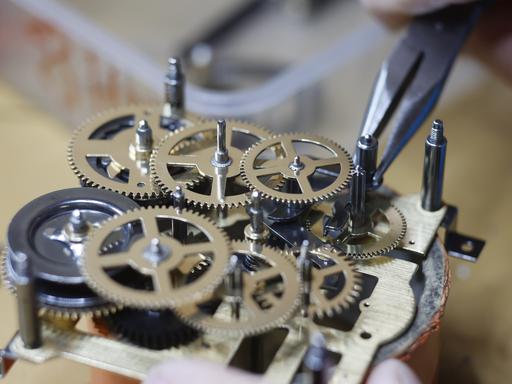Zu sehen ist die Zange eines Uhrmachermeisters, der die Zahnräder eines Uhrwerks einstellt. 