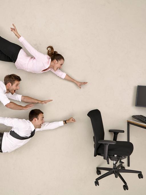 Drei Büromenschen fliegen lachend auf einen Schreibtisch mit Computer zu.