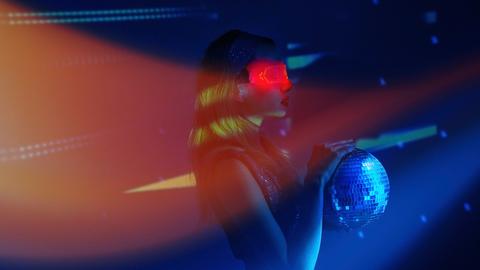 Das diffuse Bild einer Frau mit schulterlangem, hellem Haar und starrem Blick zeigt sie in einem Nachtclub mit einer rot leuchtenden VR-Brille und einer Discokugel.