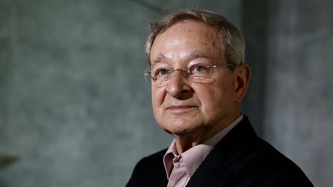 Porträtaufnahme von Péter Nádas vor einer grün-grauen Wand. Porträtaufnahme von Péter Nádas vor einer grün-grauen Wand.