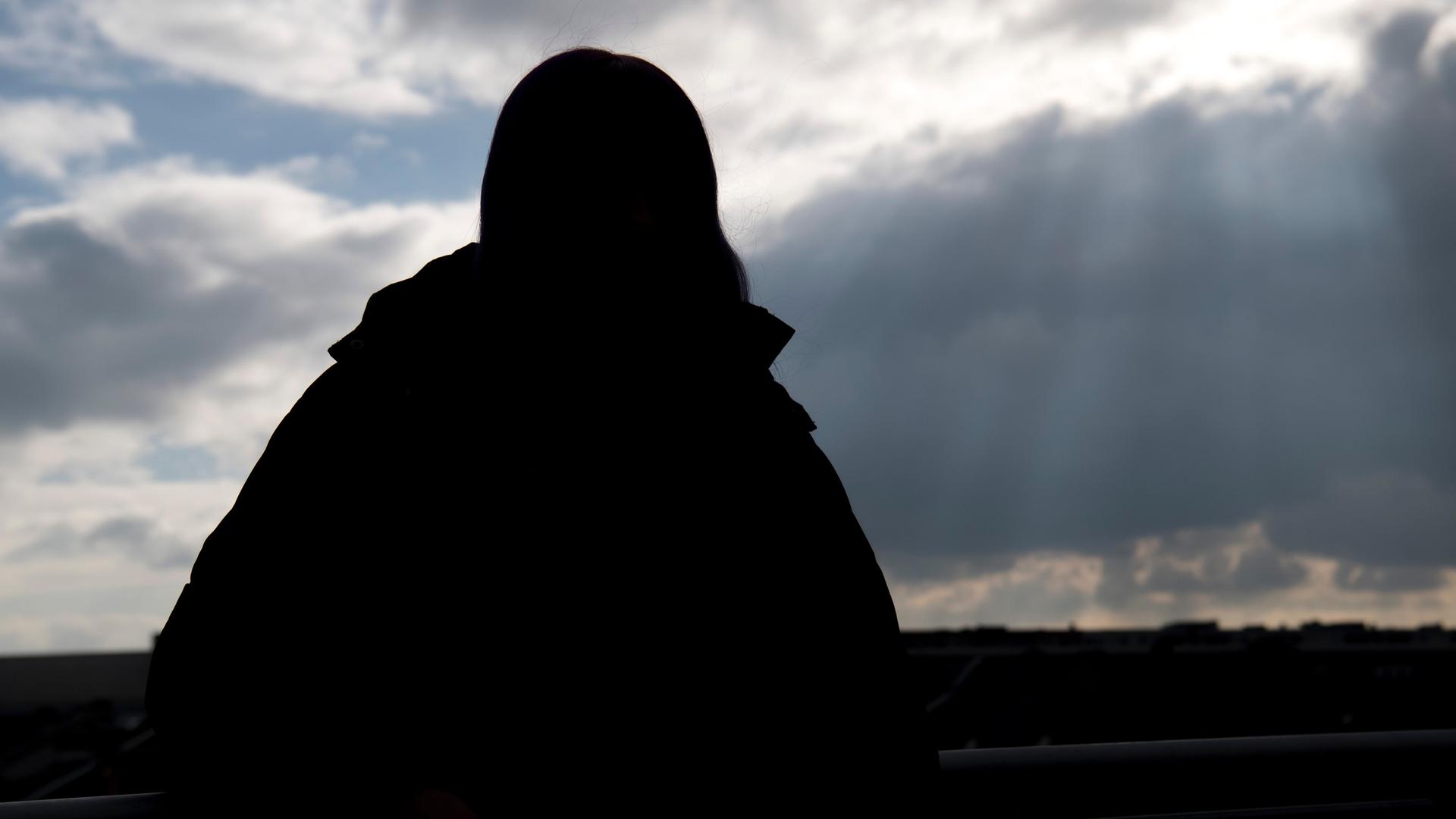 Eine junge, wohnungslose Frau in Frankfurt am Main ist im Gegenlicht nur als Silhouette erkennbar.